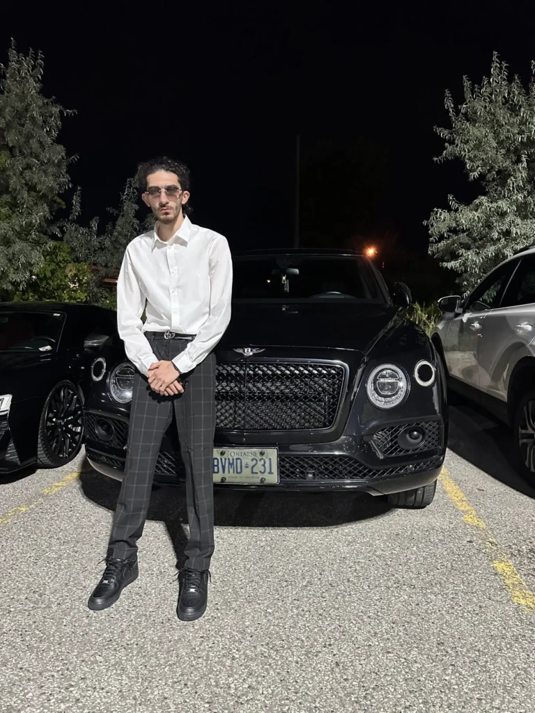 Professional master barber and shop owner standing in front of a luxury black SUV at night.